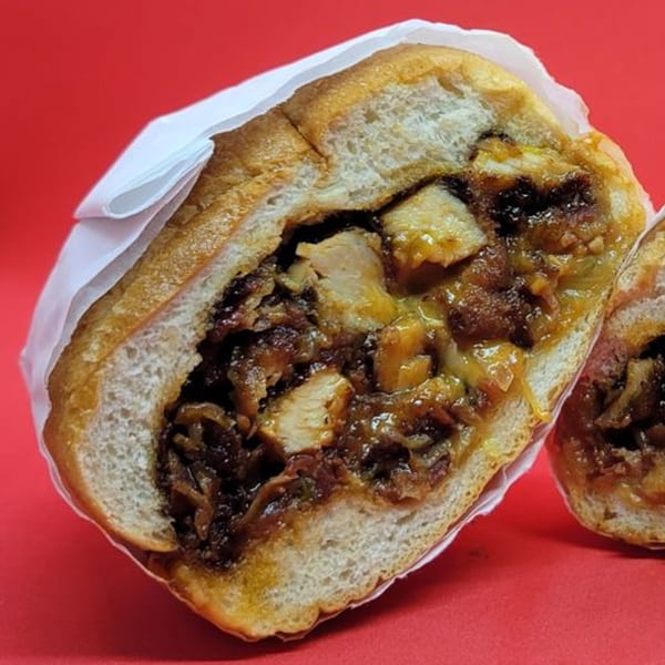 A Notable Jamaican jerk chicken sandwich, cut in half, revealing savory filling on a red background.