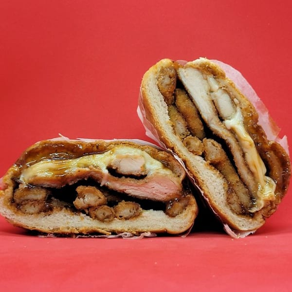 Two halves of a Jamaican sandwich, filled with fried chicken, cheese, and gravy, on a red background.