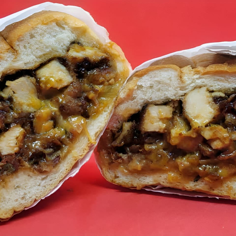 Two halves of a Jamaican jerk chicken sandwich with rich sauce on a red background.