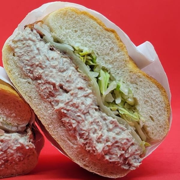 A Notable Jamaican sandwich with creamy filling, lettuce, and onions on a bun, against a red background.