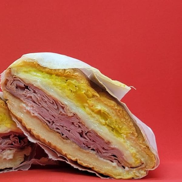 A Notable Jamaican sandwich, cut in half, revealing layers of meat, cheese, and yellow filling.