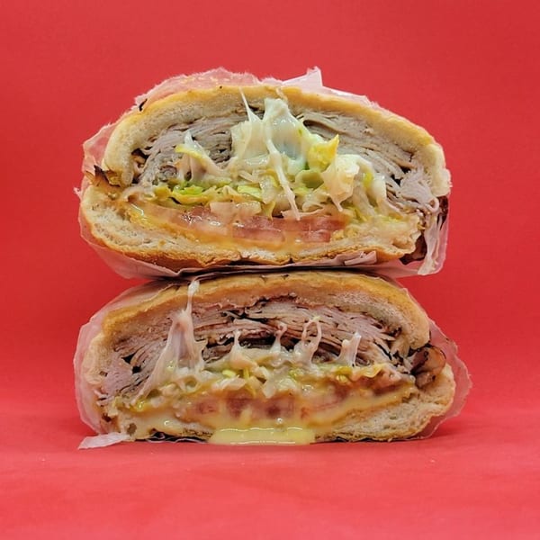 Two halves of a Jamaican sandwich, filled with meat, cheese, lettuce, and tomato, on a red background.