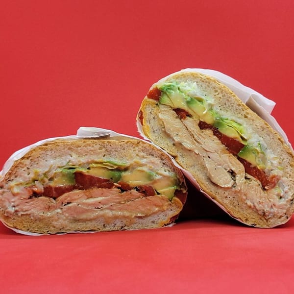 Two halves of a Notable Jamaican sandwich with chicken, avocado, and tomato on a red background.