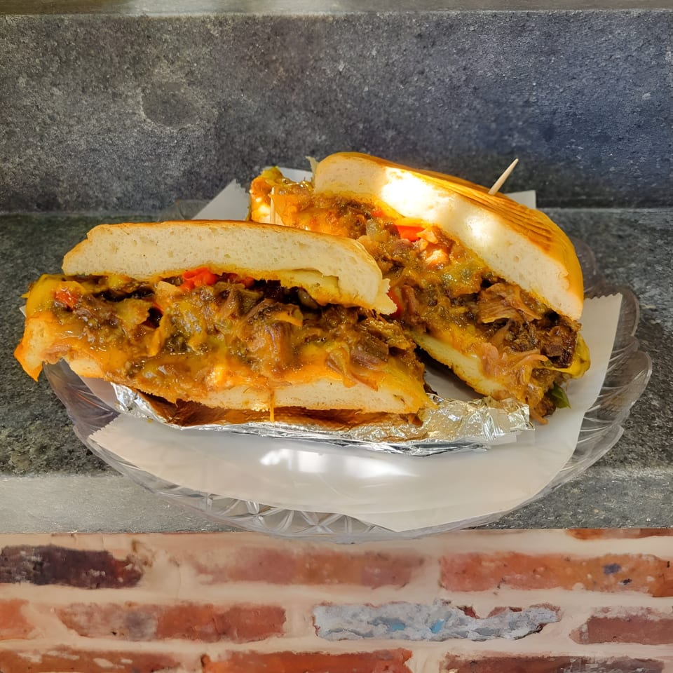 Two halves of a Notable Jamaican jerk chicken sandwich with melted cheese and peppers on a plate.